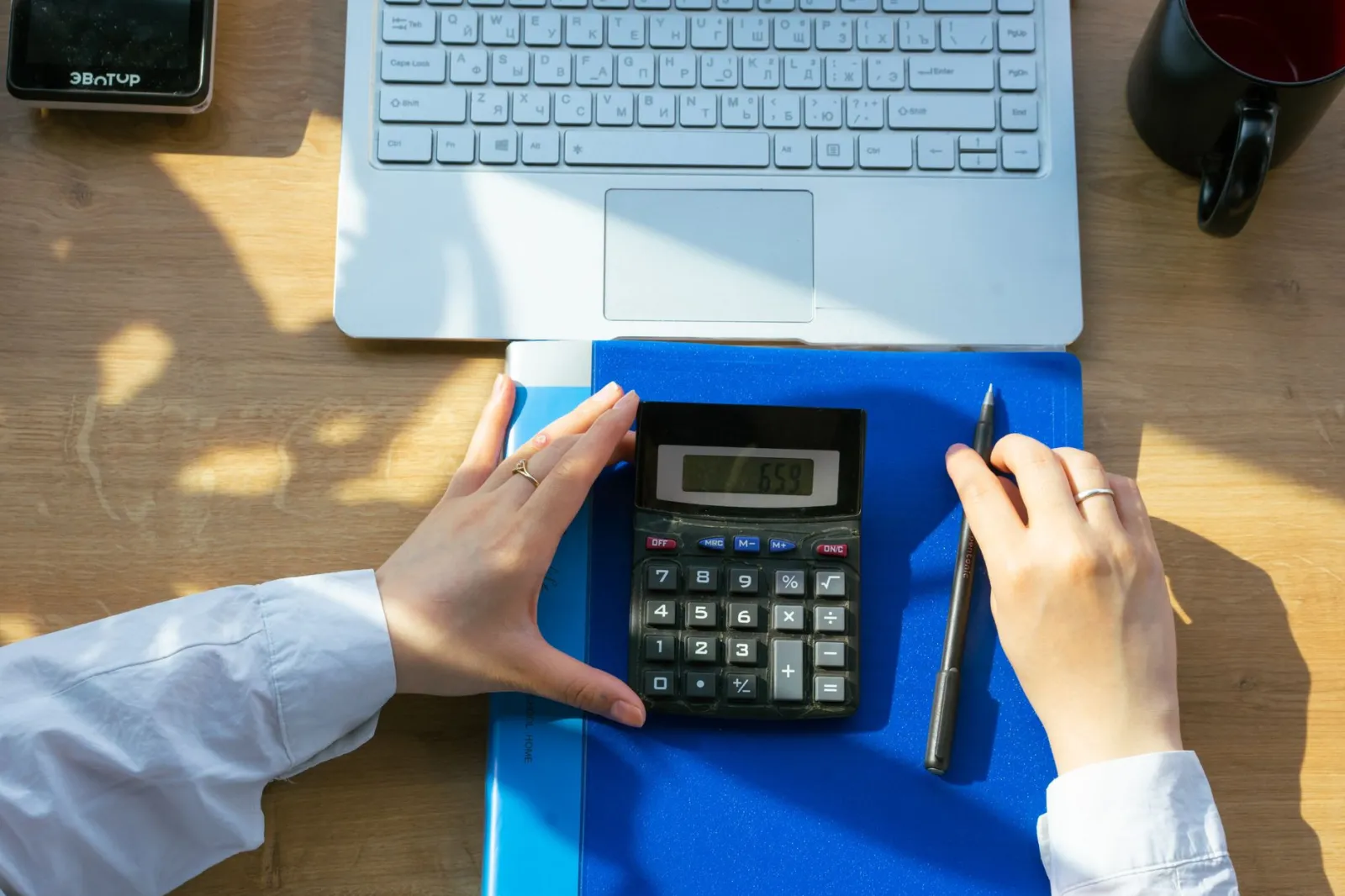 Hands using calculator on a desk with a laptop, pen, and notebook. Perfect for office or finance themes.
